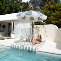 A woman relaxes on a striped poolside lounger under the Mentari Market Umbrella in Sage and oat